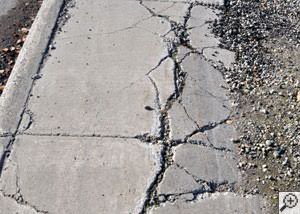 A severely damaged, sinking sidewalk with washed out sand underneath in Peterborough.