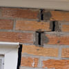 A brick wall displaying stair-step cracks and messy tuckpointing on a Hamilton home